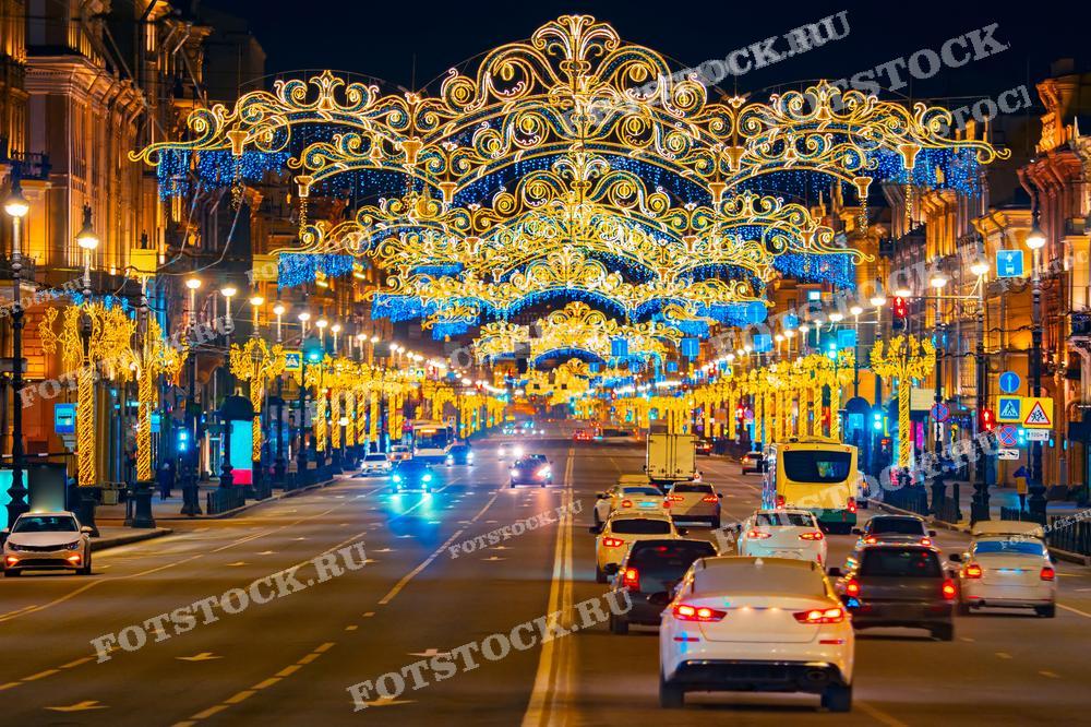 На фотографии запечатлен Невский проспект в Санкт-Петербурге, украшенный праздничной новогодней иллюминацией. Видны ослепительные световые гирлянды, создающие эффект праздничного купола над дорогой. Многочисленные автомобили освещают дорогу, создавая динамичное ощущение городской жизни. Такой снимок идеально подойдёт для статей о городской культуре и праздниках, для использования в качестве открыток или плакатов, а также может служить украшением для интерьеров или веб-страниц, посвящённых зимним праздникам.